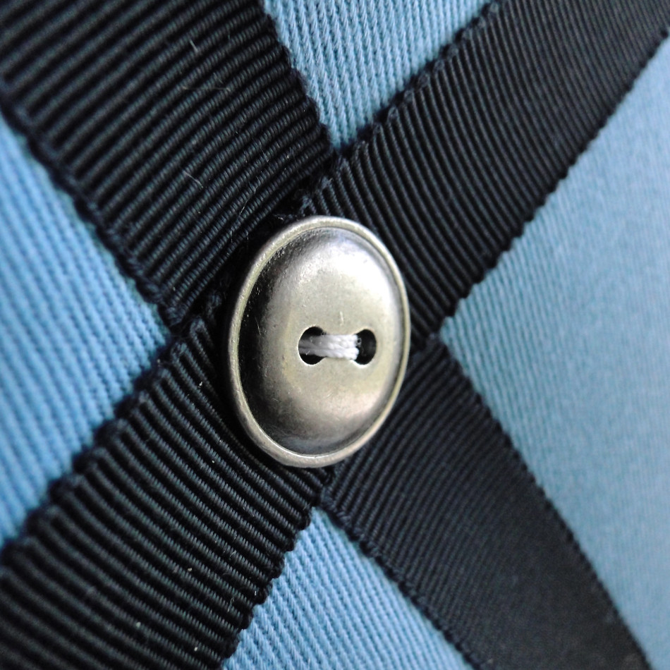 Close-up of navy ribbon and antique nickel button details on blue cotton fabric